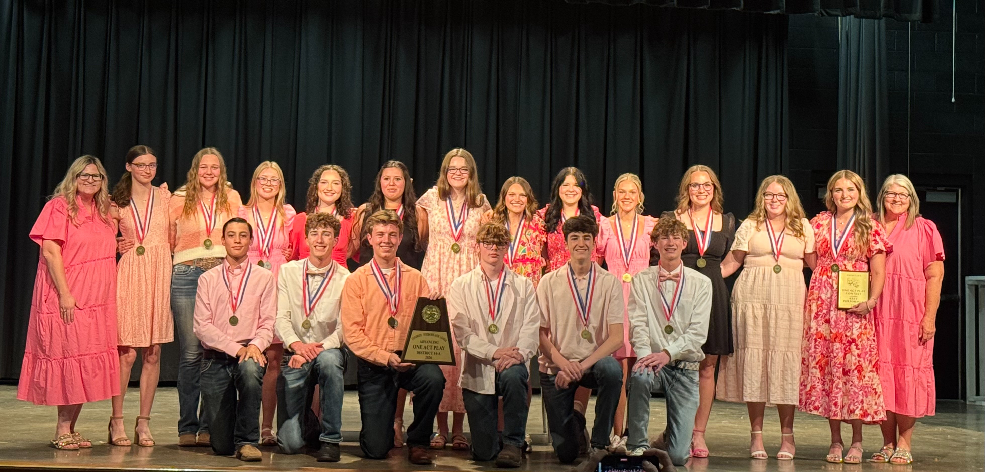Students in cast in costume in a group photo on stage.