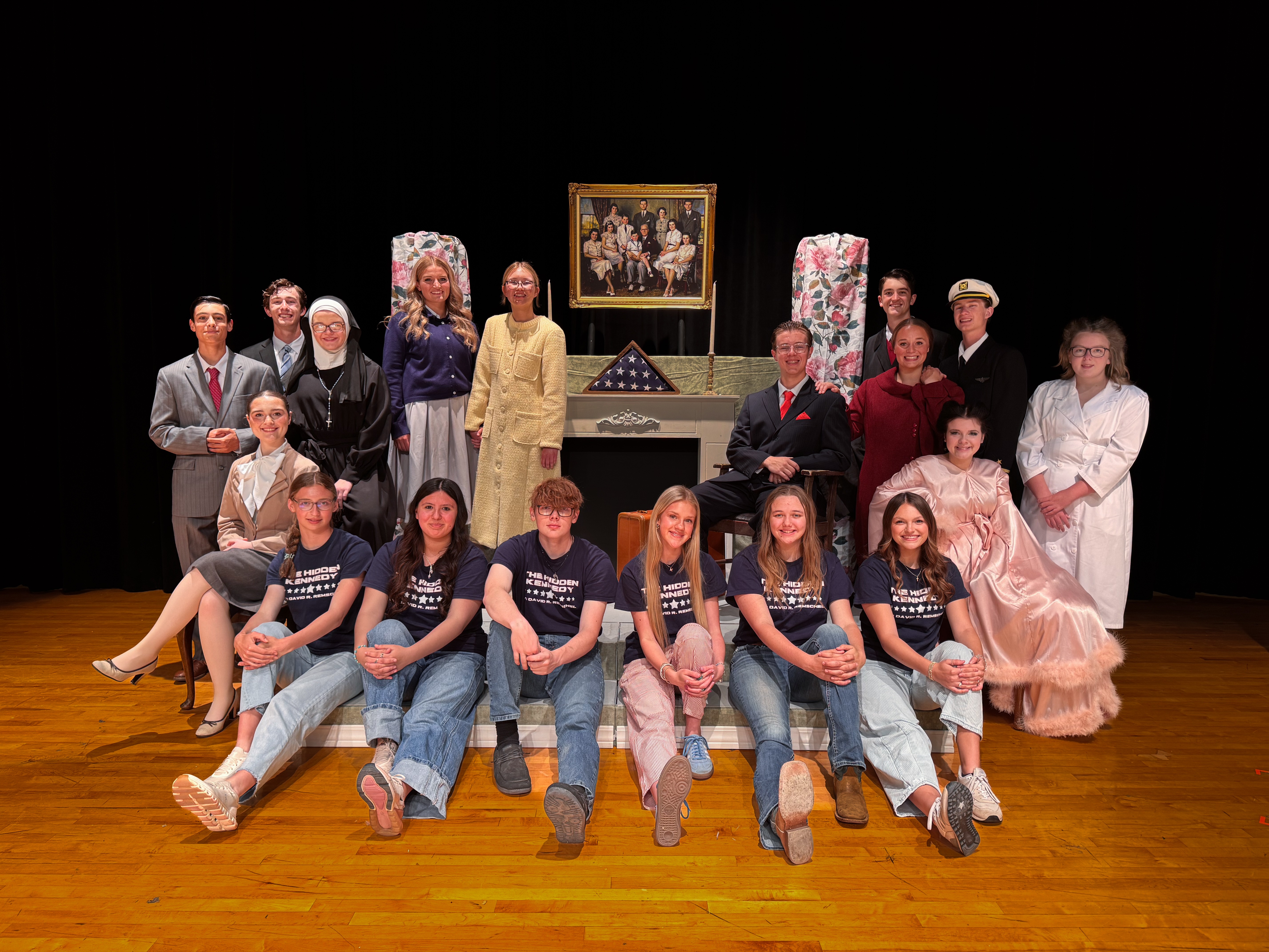 Students in cast in costume in a group photo on stage.