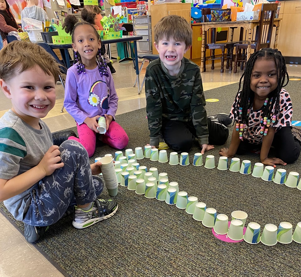 Four children sitting in classroom with cups laid out in front of them