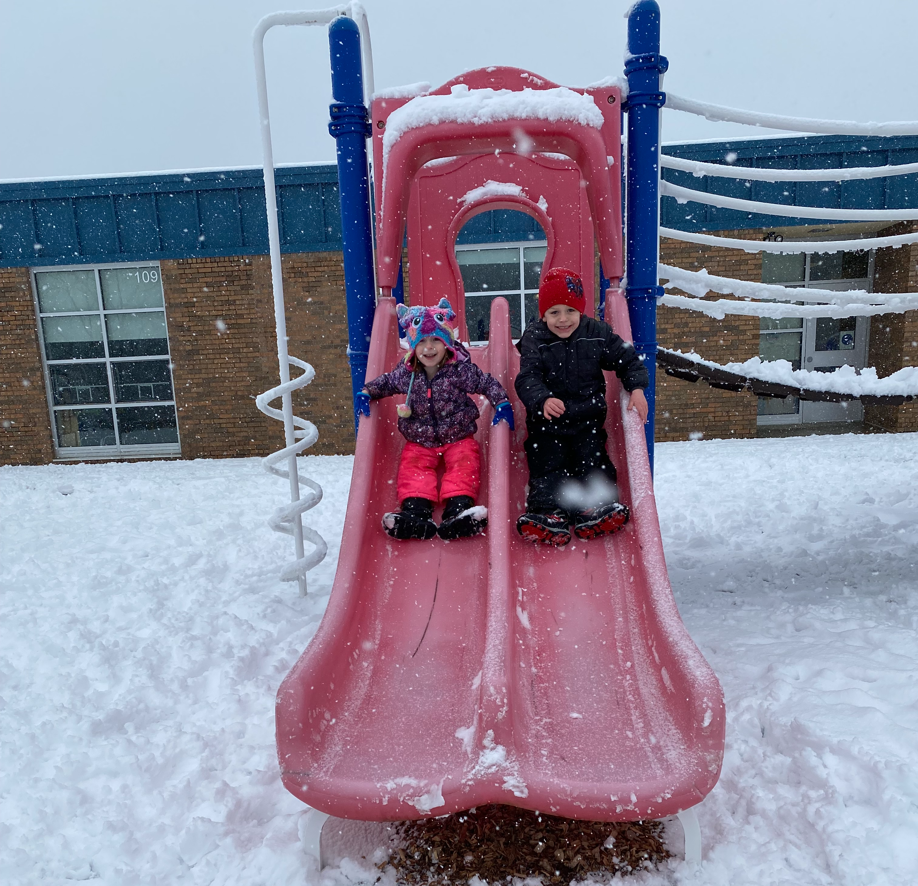 Two children going down a slide in the snow