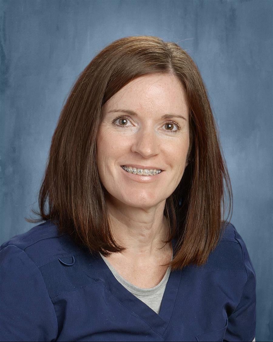 A woman with shoulder length brown hair smiling against a navy blue photography background.