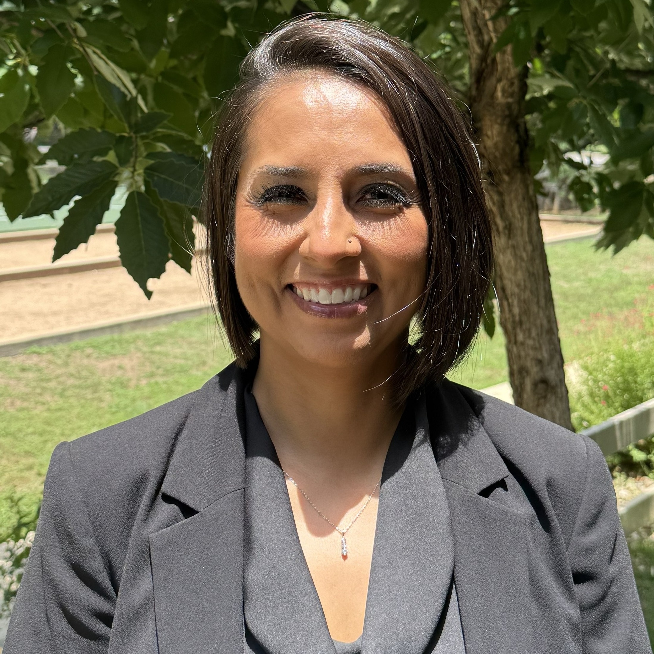 A woman with shoulder length brown hair wearing black jacket and shirt while smiling.