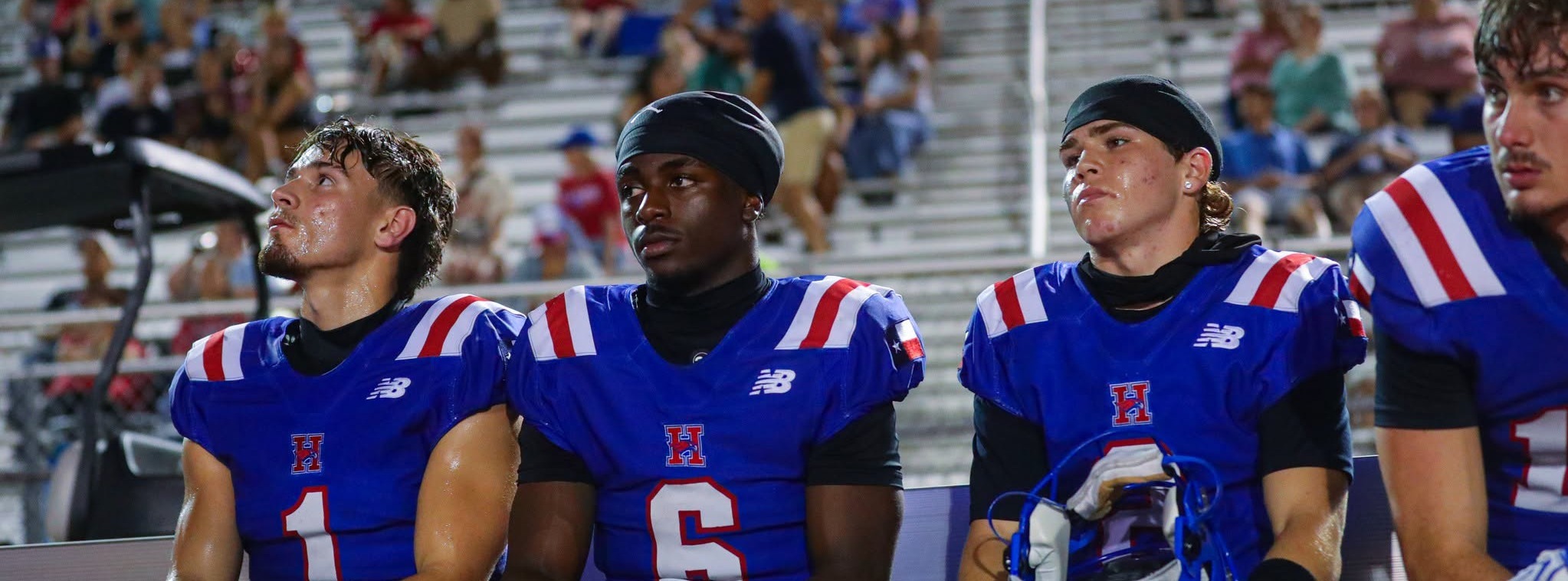 Four varsity football players looking off in the distance while sitting on the bench during a game.