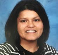 A smiling woman with shoulder length black hair in front of a blue professional photography background 