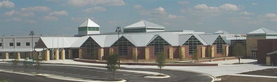 A modern educational building featuring a unique architectural design with multiple peaked roofs and large windows, set against a partly cloudy sky.