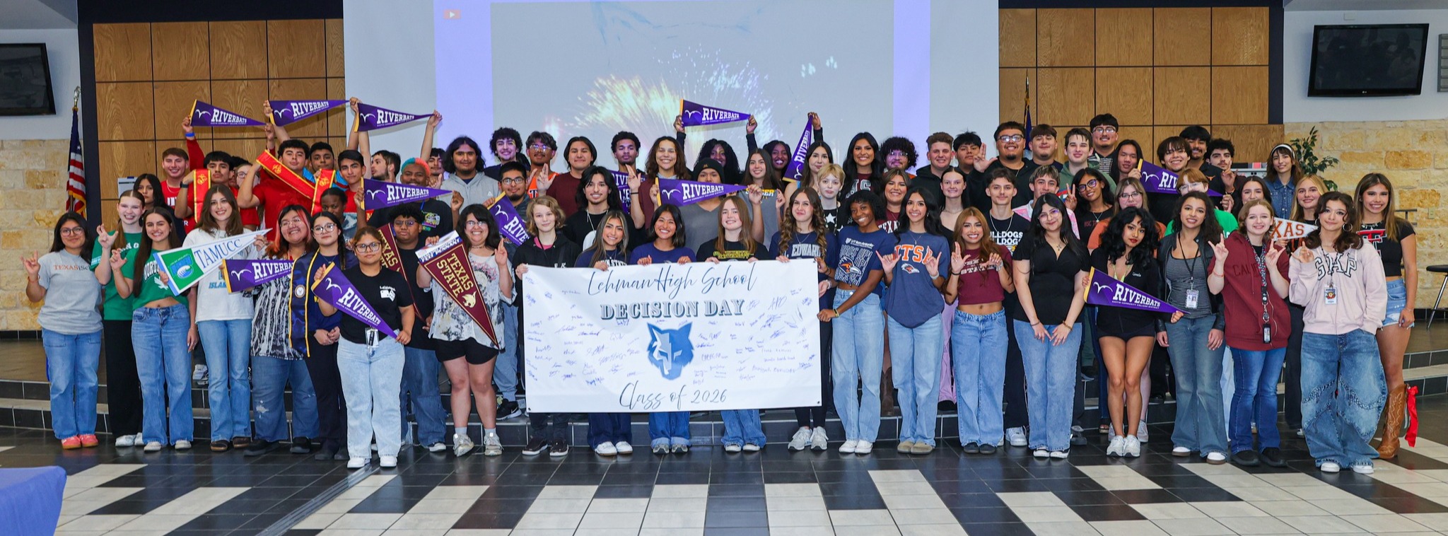 A large group of Lehman High School students standing together for a group photo while students showcase college flags.