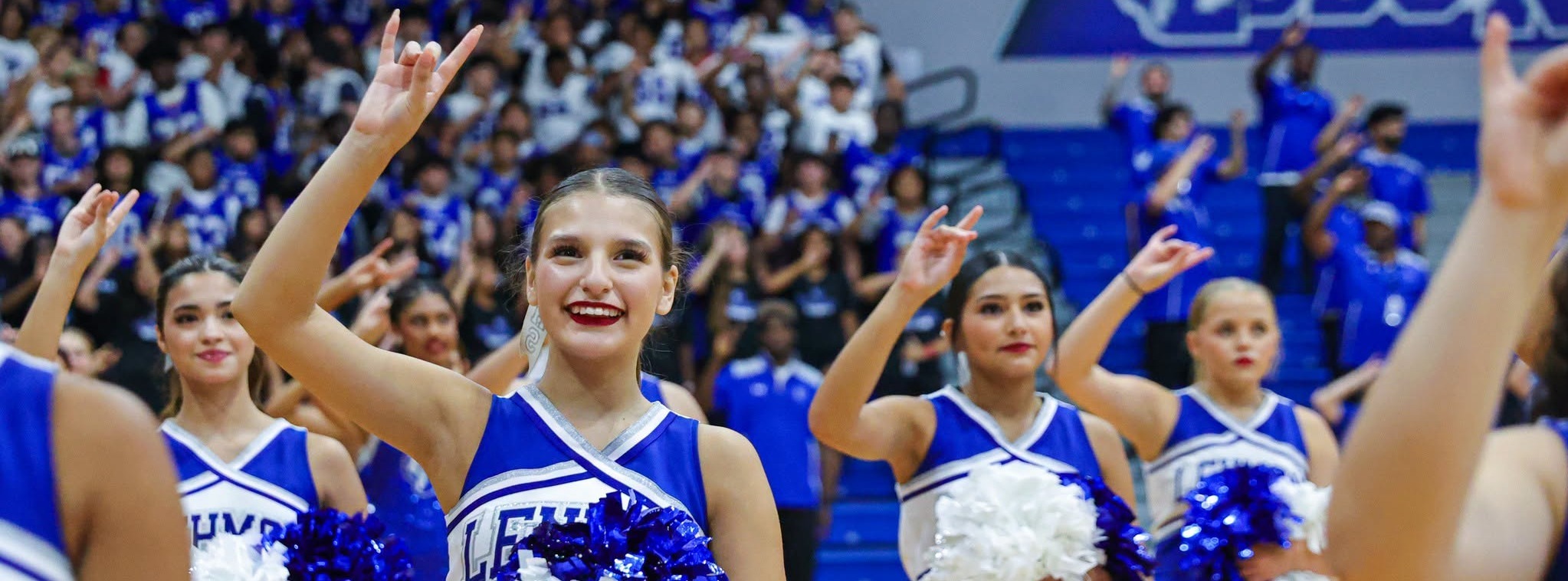 Cheerleaders with students in the background doing their school symbol