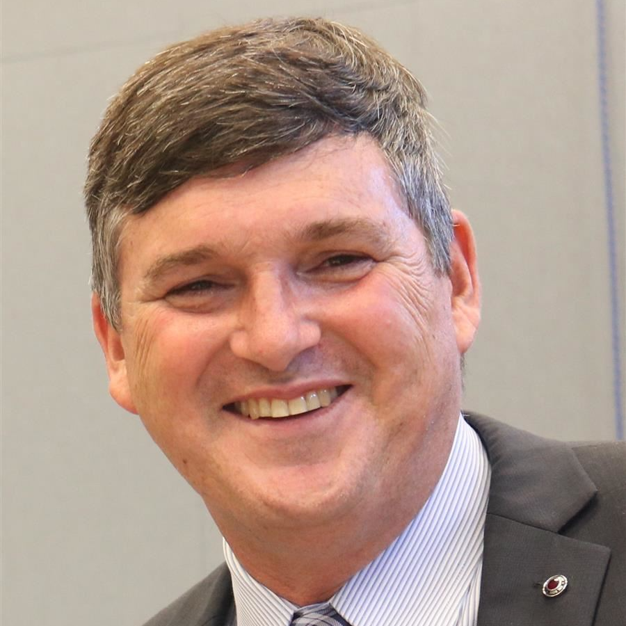 A man with short graying hair in a gray suit jacket and striped shirt smiling.