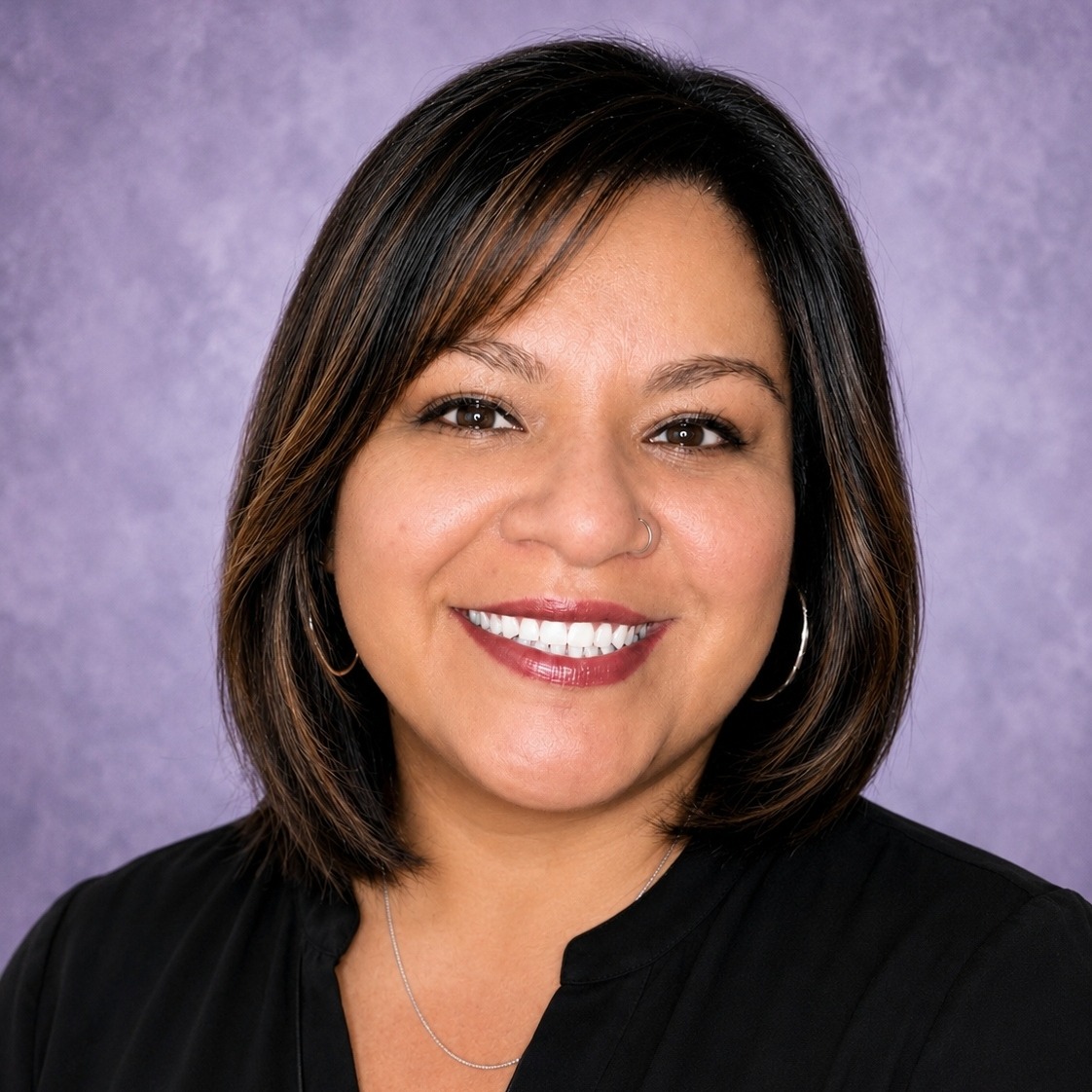 A smiling woman with short, dark hair, wearing a black top, against a violet background.
