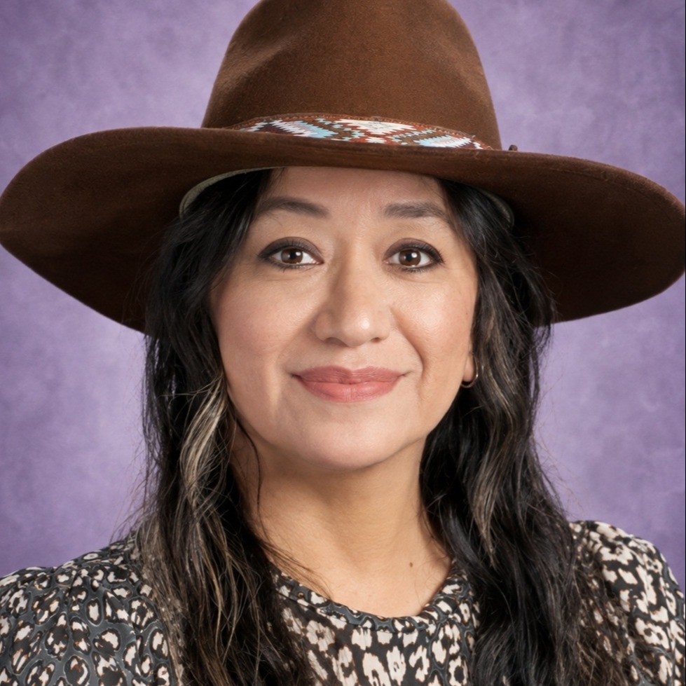 A woman with long, straight hair wearing a hat and a black and white top against a violet background..