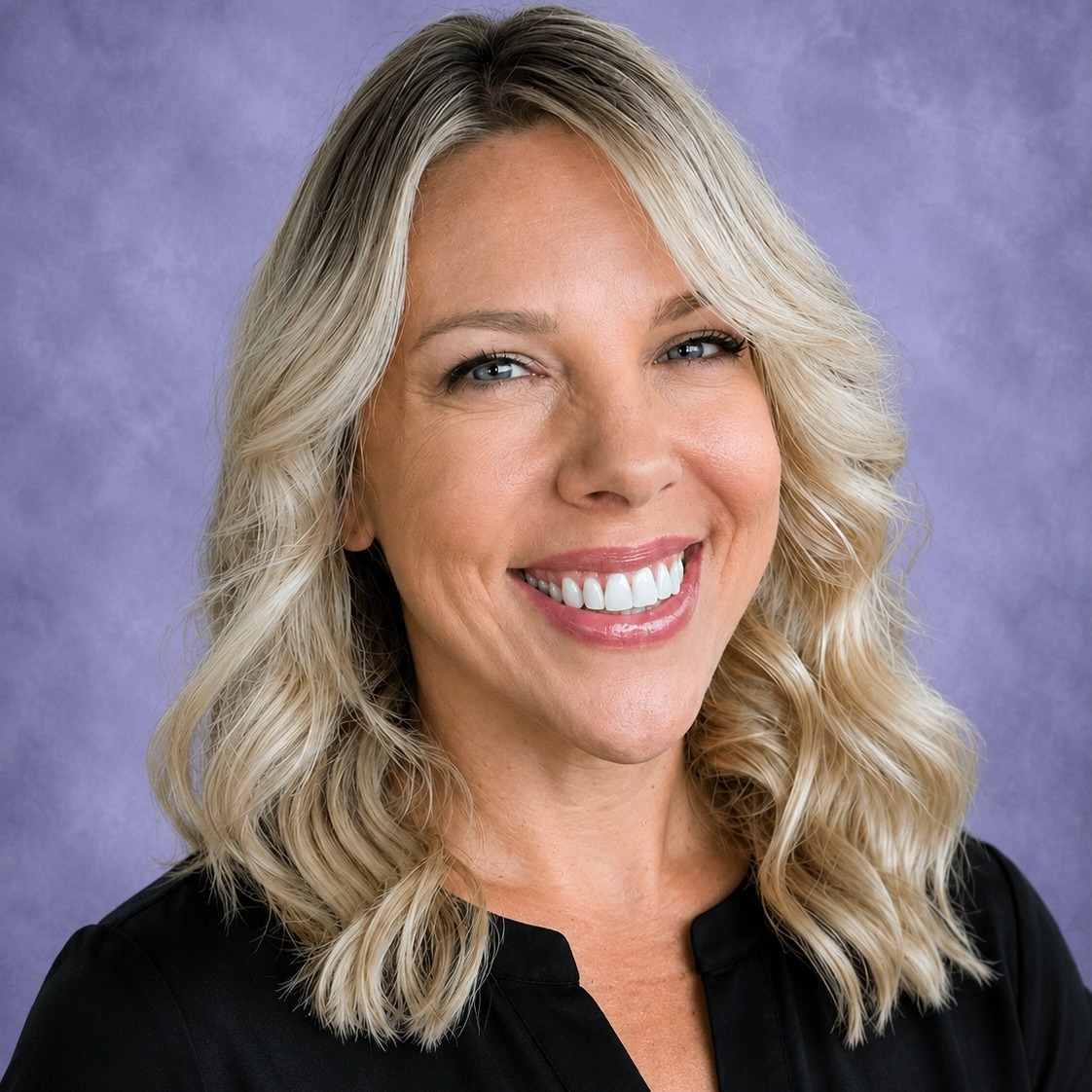 A smiling woman with blond hair, wearing a black top, against a violet background.