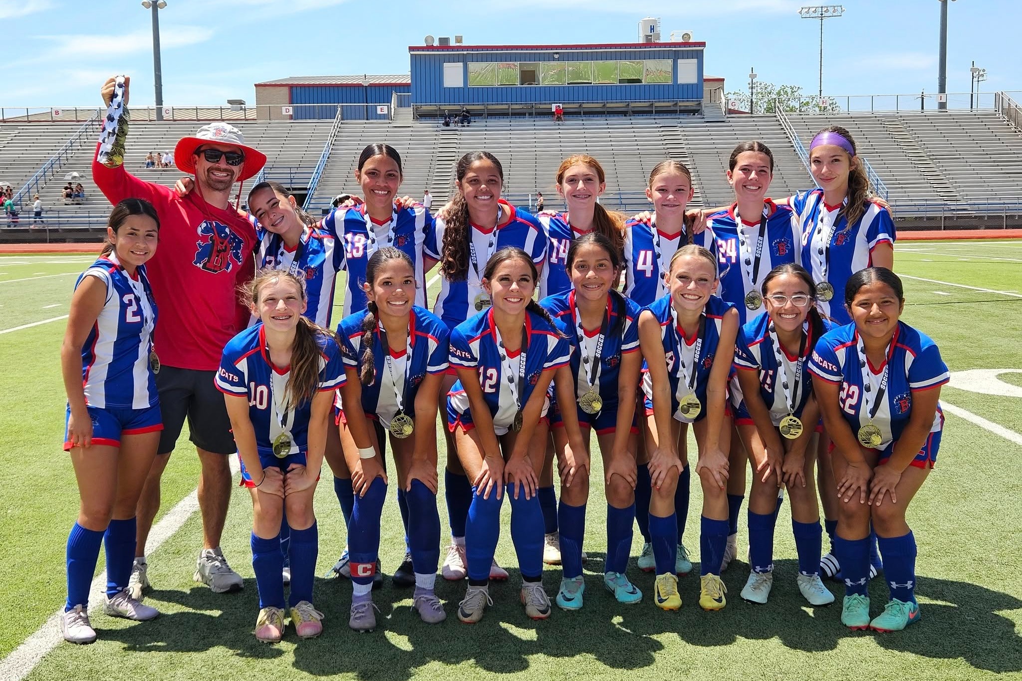A group of female BMS soccer athletes posing for a group photo with their coach .