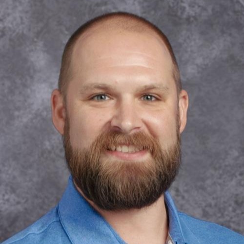 A smiling man with short hair in a blue shirt against a grey background.