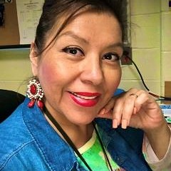 A smiling woman with her hair up in a ponytail and wearing a blue jacket with a yellow and green shirt.