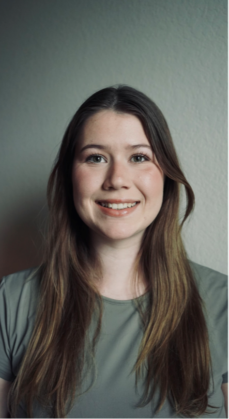 A smiling woman with long brown hair wearing a gray shirt.