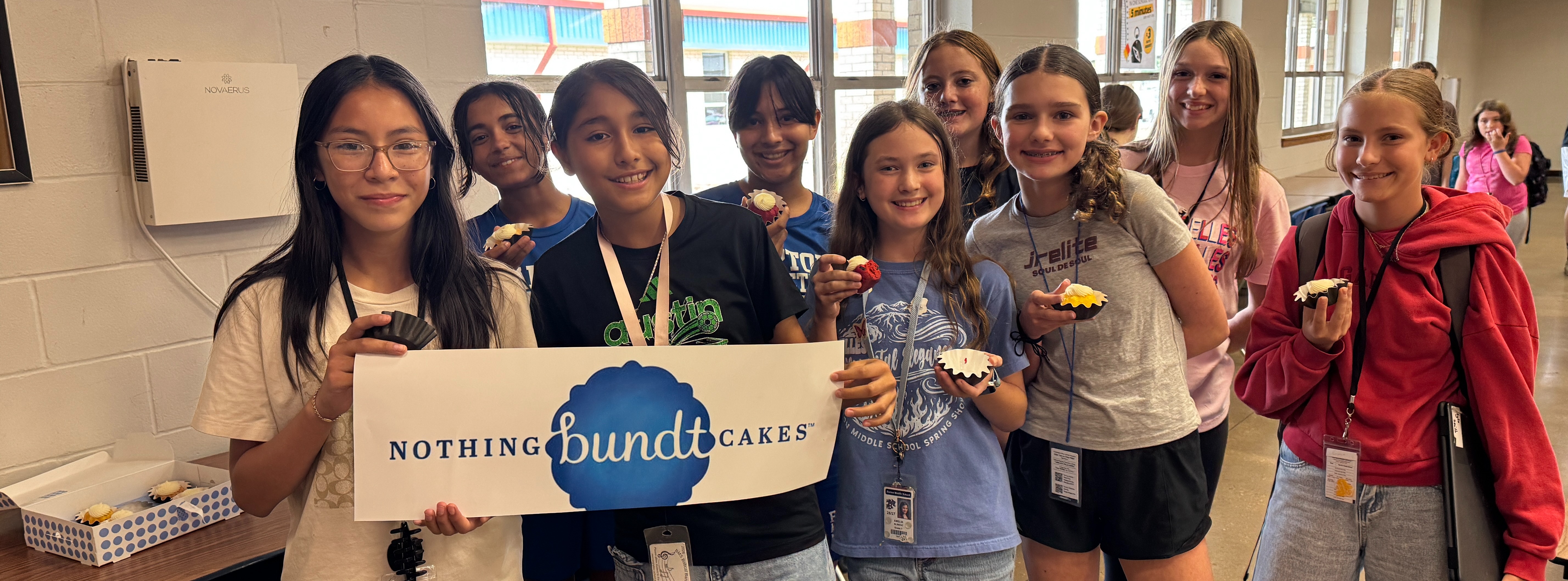 A group of students with cupcakes in their hands while some students are carrying a banner for Nothing Bundt Cakes.