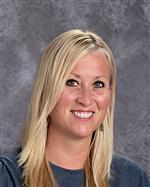 A smiling woman with long blonde hair, wearing a gray top, poses for a professional photo against a textured gray background.