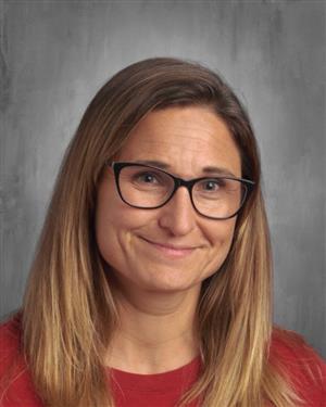 A smiling woman with long, straight hair and glasses, wearing a red shirt, poses for a professional headshot against a gray background.