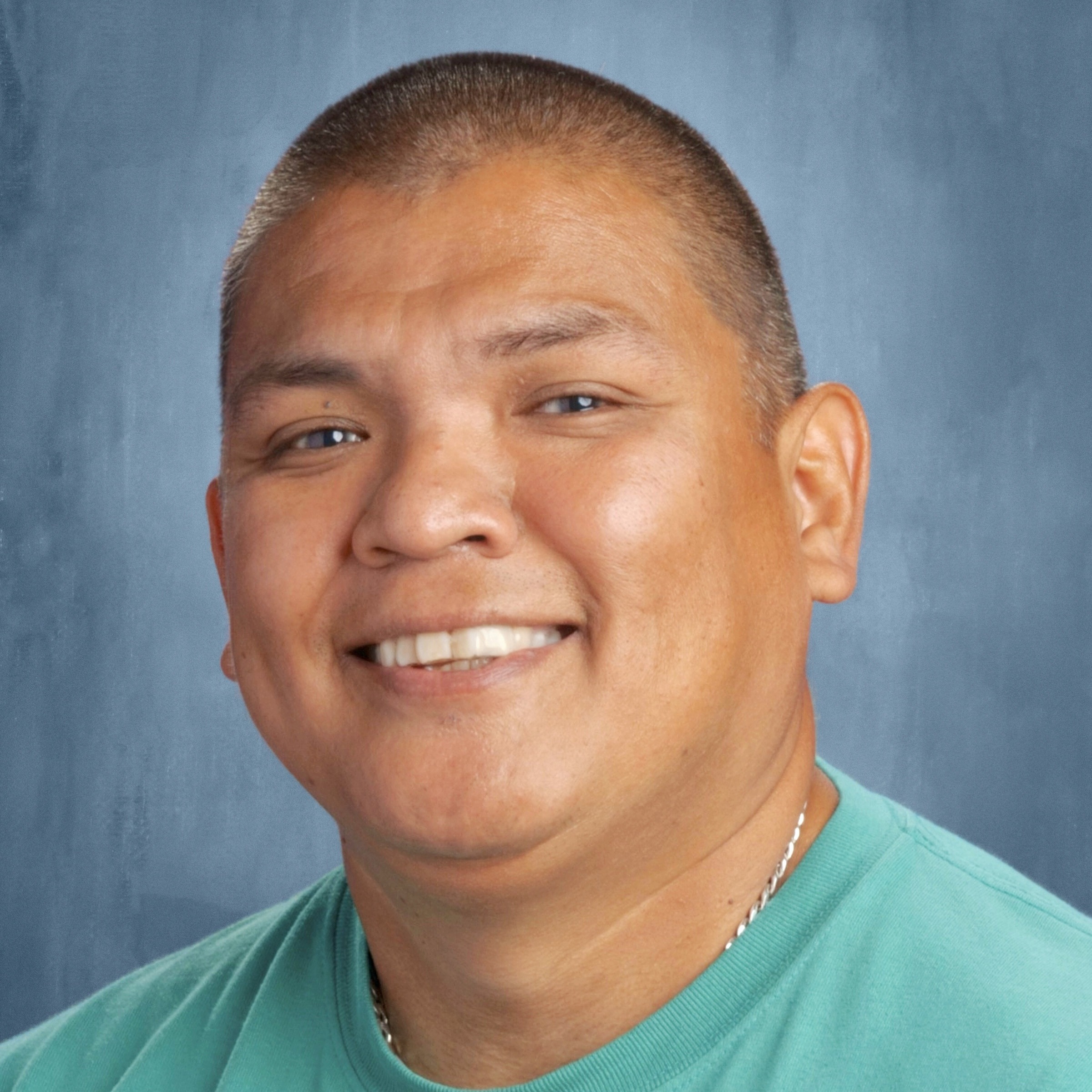 A smiling man with short hair and wearing a turquoise shirt