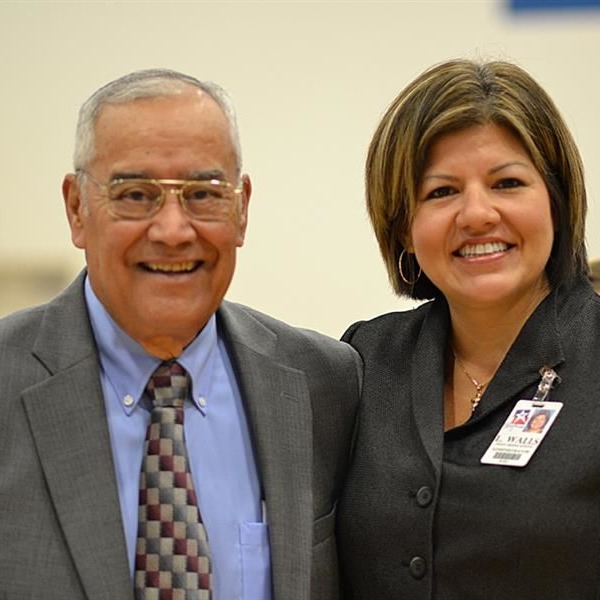 A man with short grey hair in glasses, a gray jacket, blue shirt and a tie with a woman with short hair and dark grey jacket smiling together.