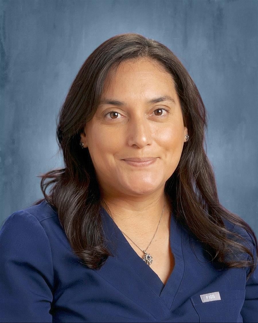 A woman with long brown hair wearing a navy blue shirt and a necklace grinning.