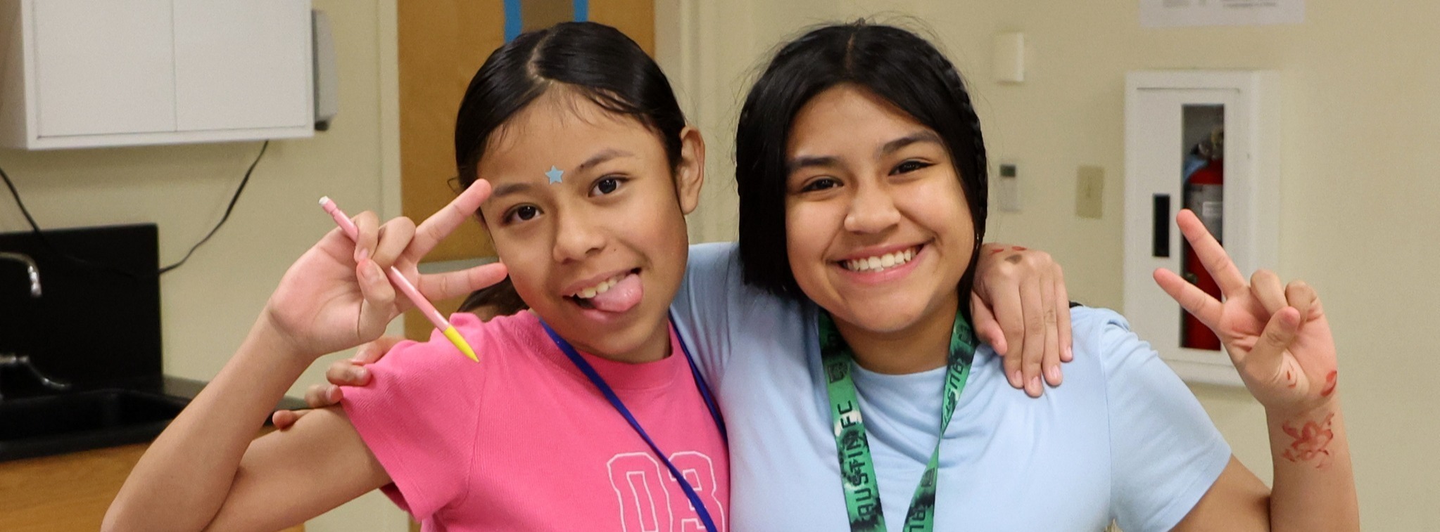 Two young girls posing at the camera while doing the peace sign with their hands.