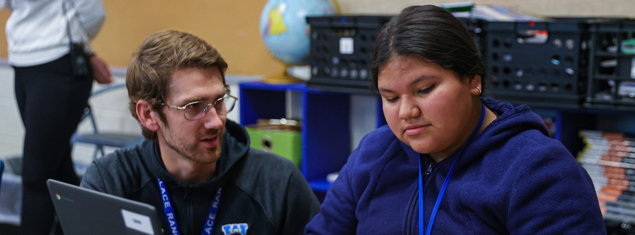 A teacher crouching next to a student and speaking to her.