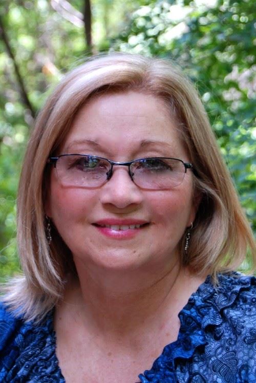 A woman with blonde hair and glasses smiling