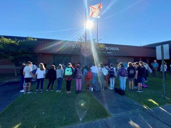 A group of students gathered around the school flagpole during sunrise on a clear day.
