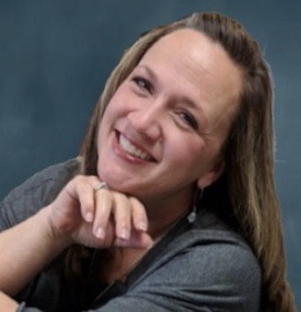 A smiling woman with long hair, resting her chin on her hand, against a blue background.