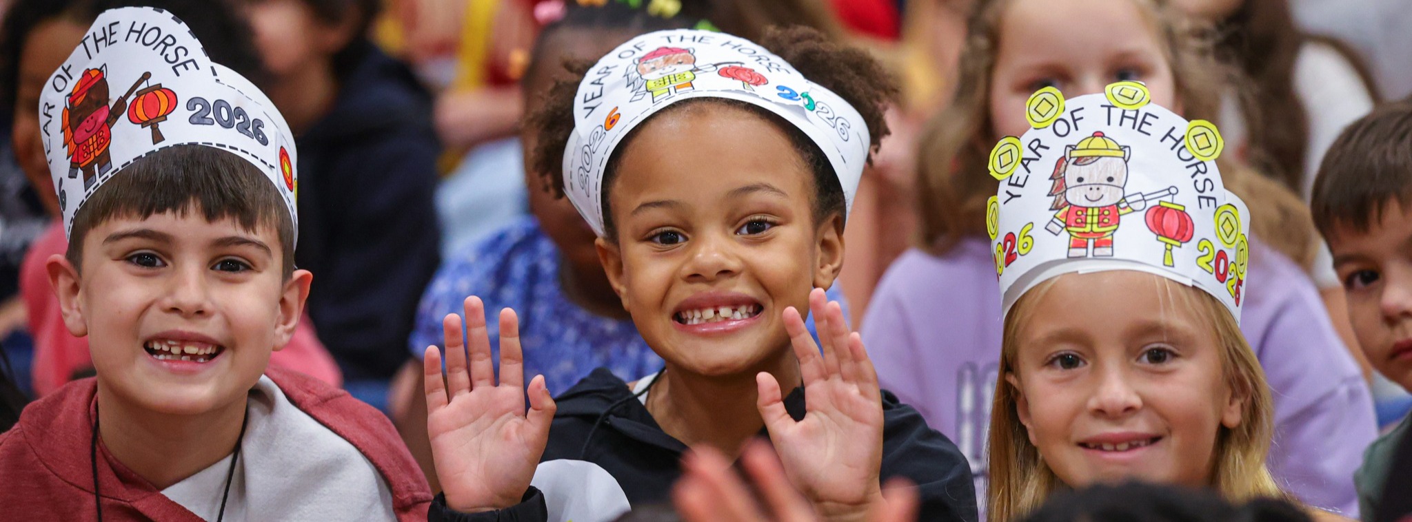 Young students celebrating  the campus Chinese New Year pep rally in the gym smiling at the camera.