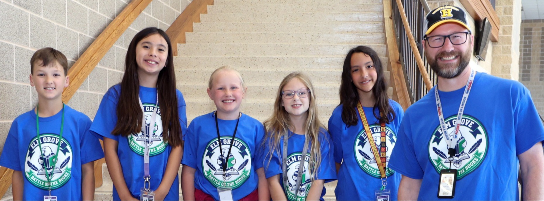 A group of five students and a teacher wearing matching blue shirts and smiling.