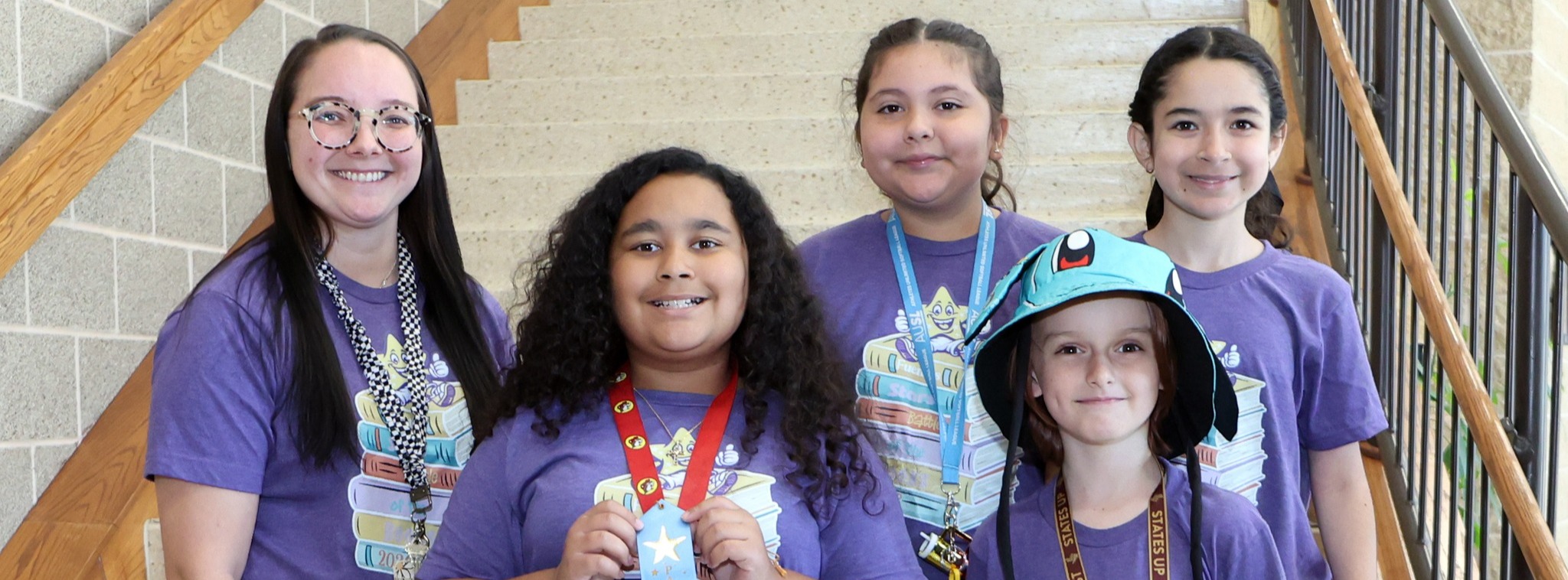 A group of four students and a teacher wearing a matching purple shirt, smiling at the camera.