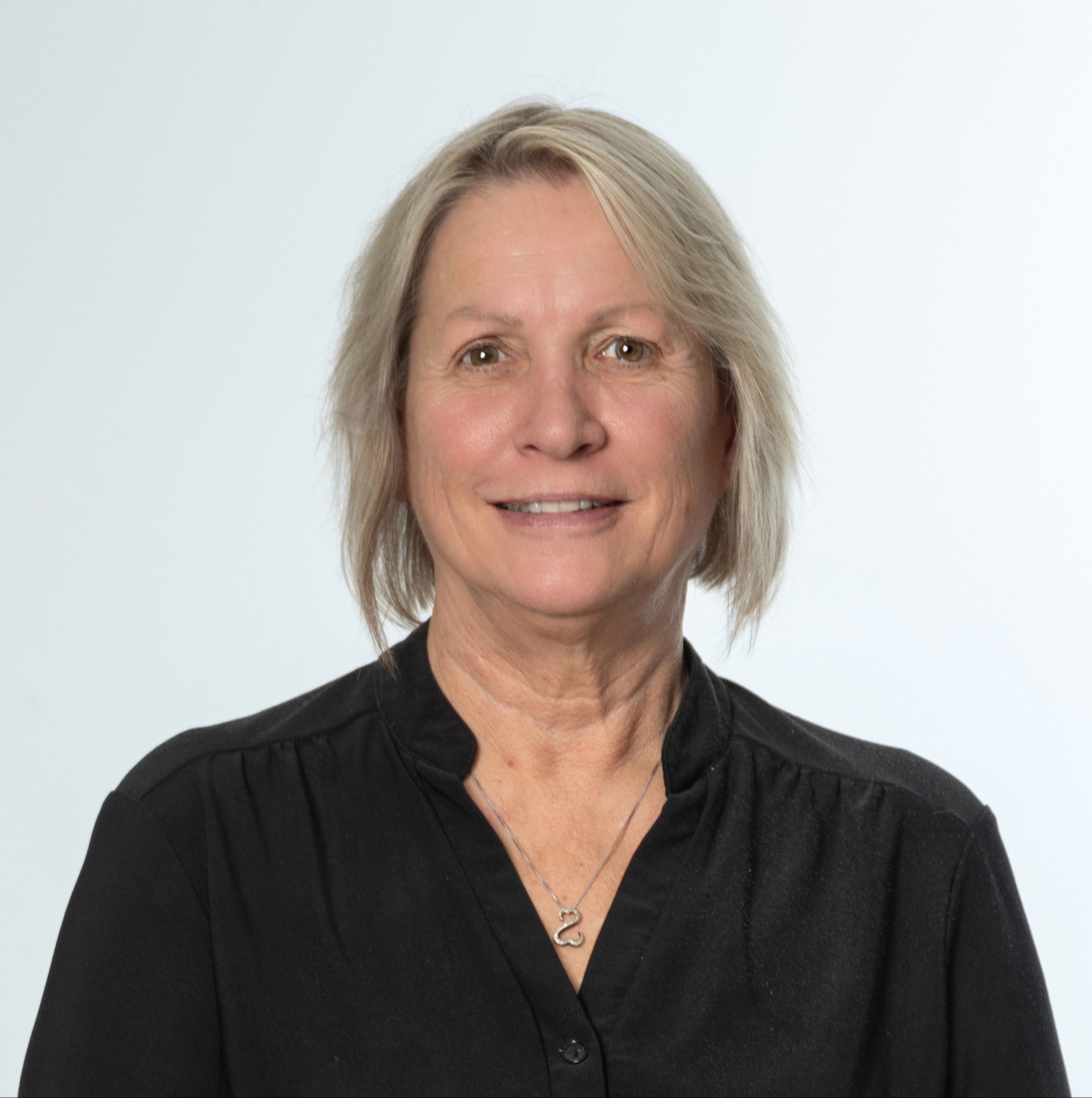 A photo of a woman with short blonde hair smiling while in front of a white background.