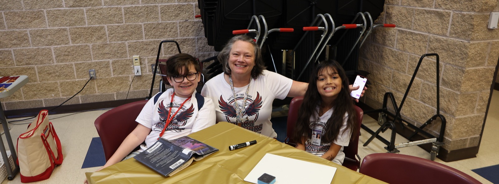 A smiling teacher between two students posing for the camera while wearing matching shirts.