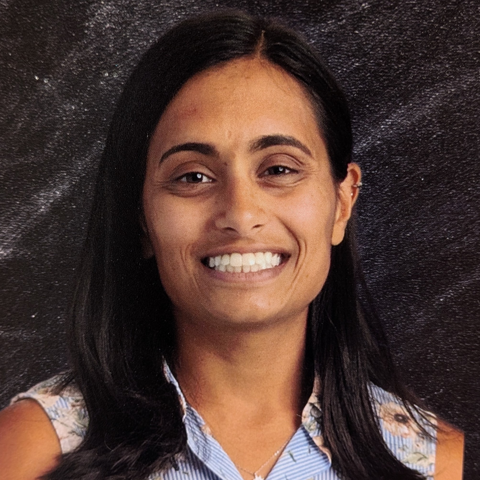 A smiling woman with long black hair wearing a floral design shirt.