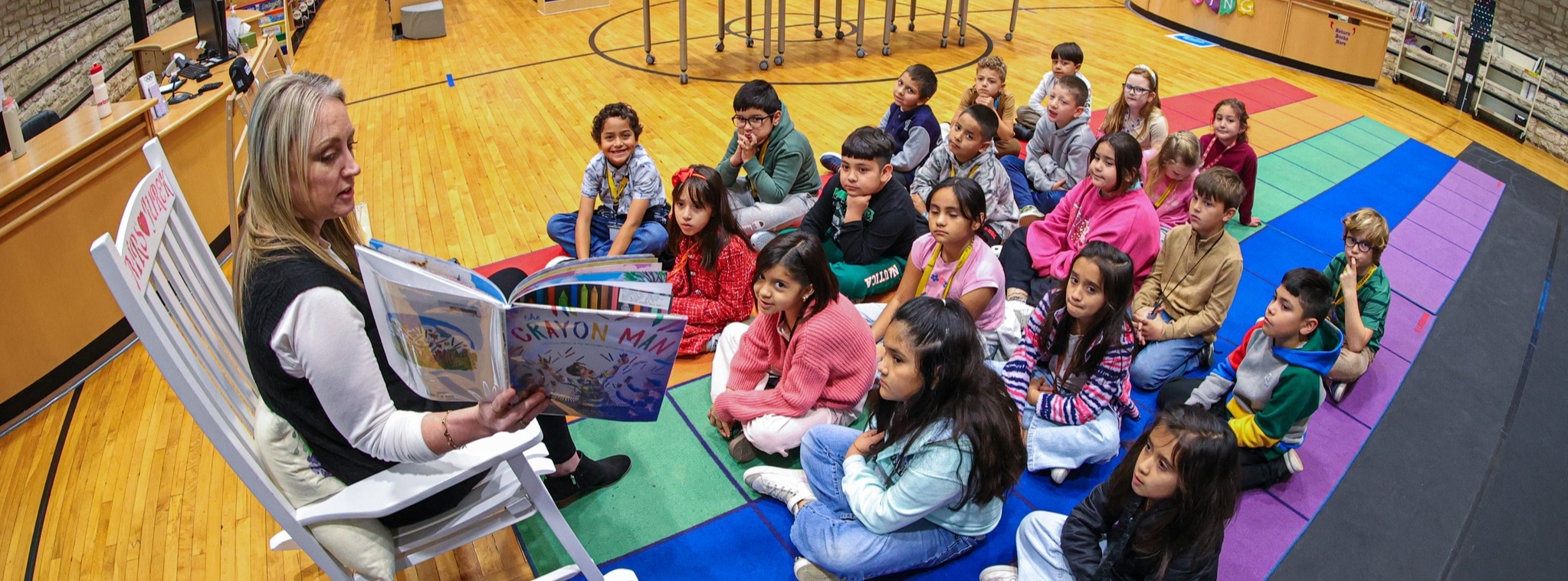 A class of Kyle Elementary students sitting in front of the librarian reading a book to them.