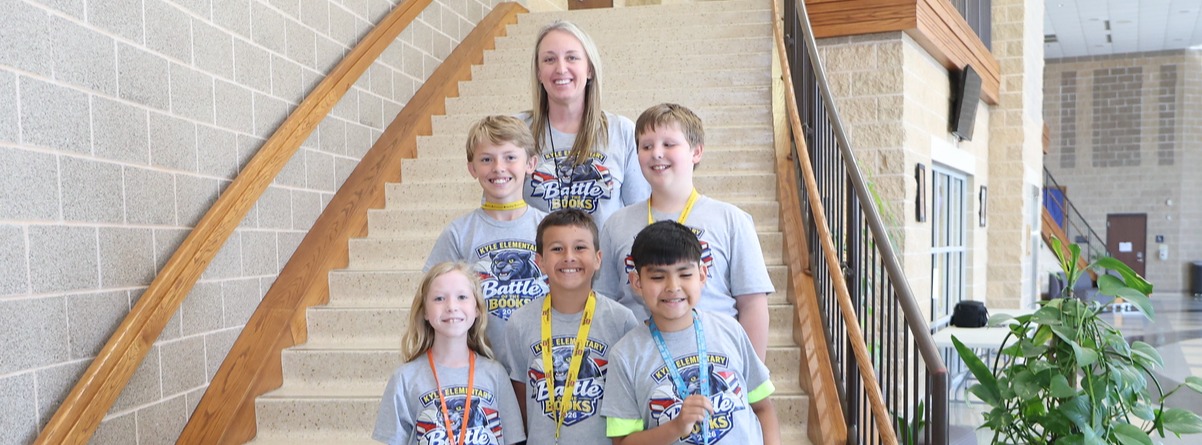 A group of five smiling students with their teacher posing for a group photo on a stairwell while wearing matching shirts.