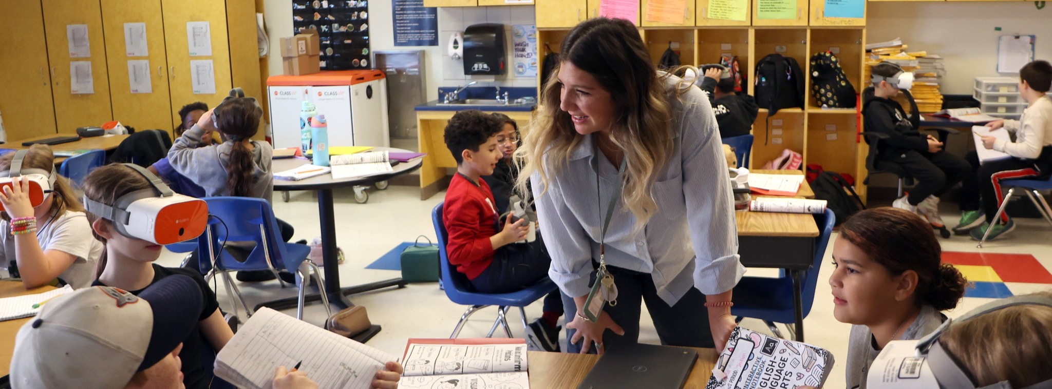 Pfluger Elementary School teacher communicating with students at a table with other students in the background doing classwork.