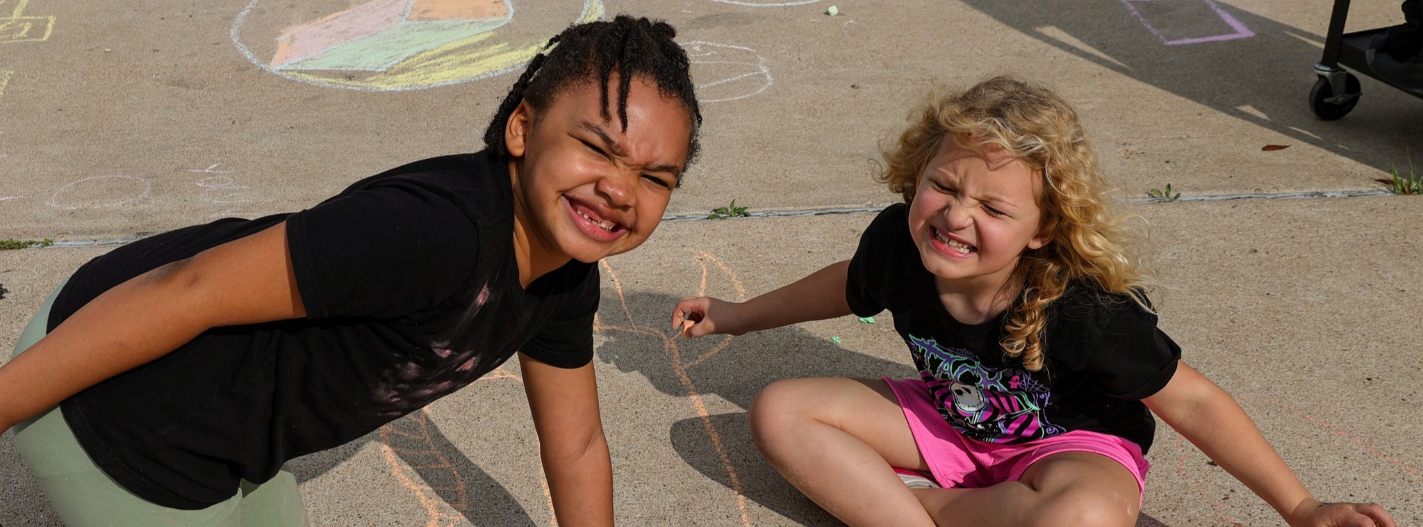 Two young girls smiling at the camera while playing with chalk