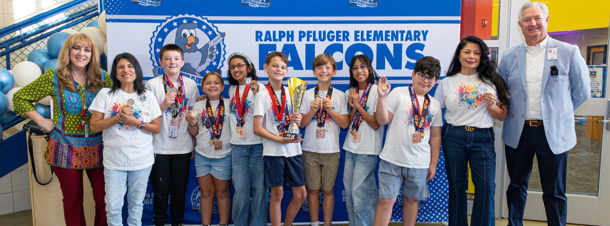 A group of adults and students standing in line together in front of a Ralph Pfluger Elementary backdrop.