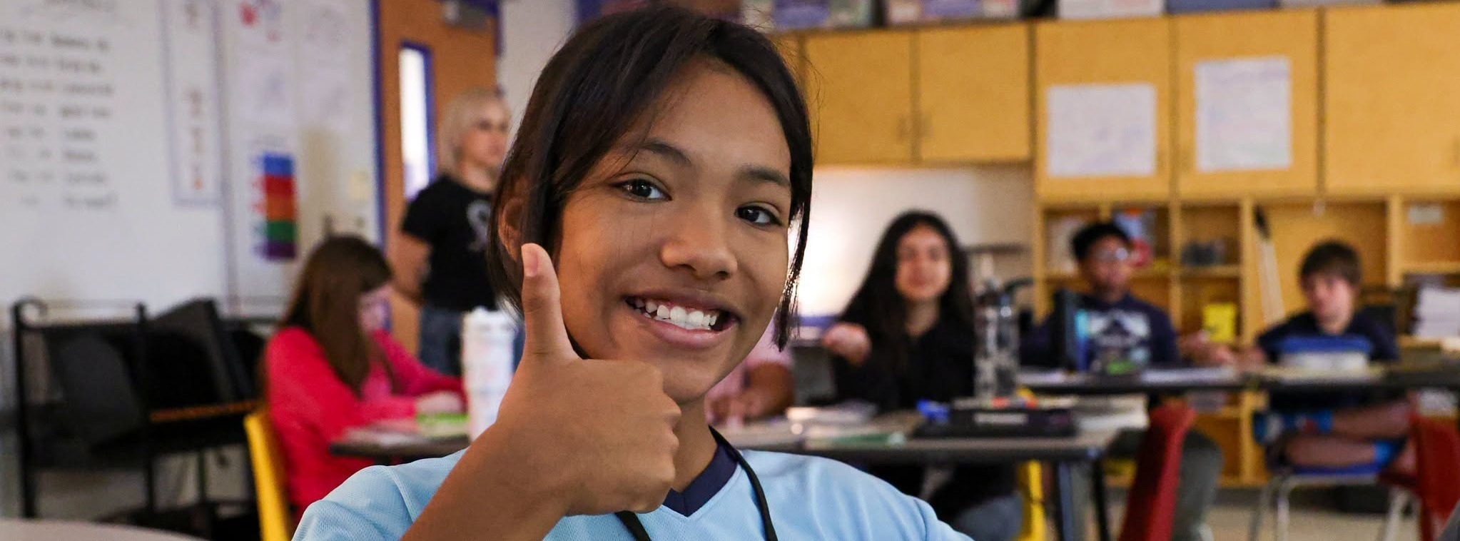 A girl giving a thumbs up and smiling during class.