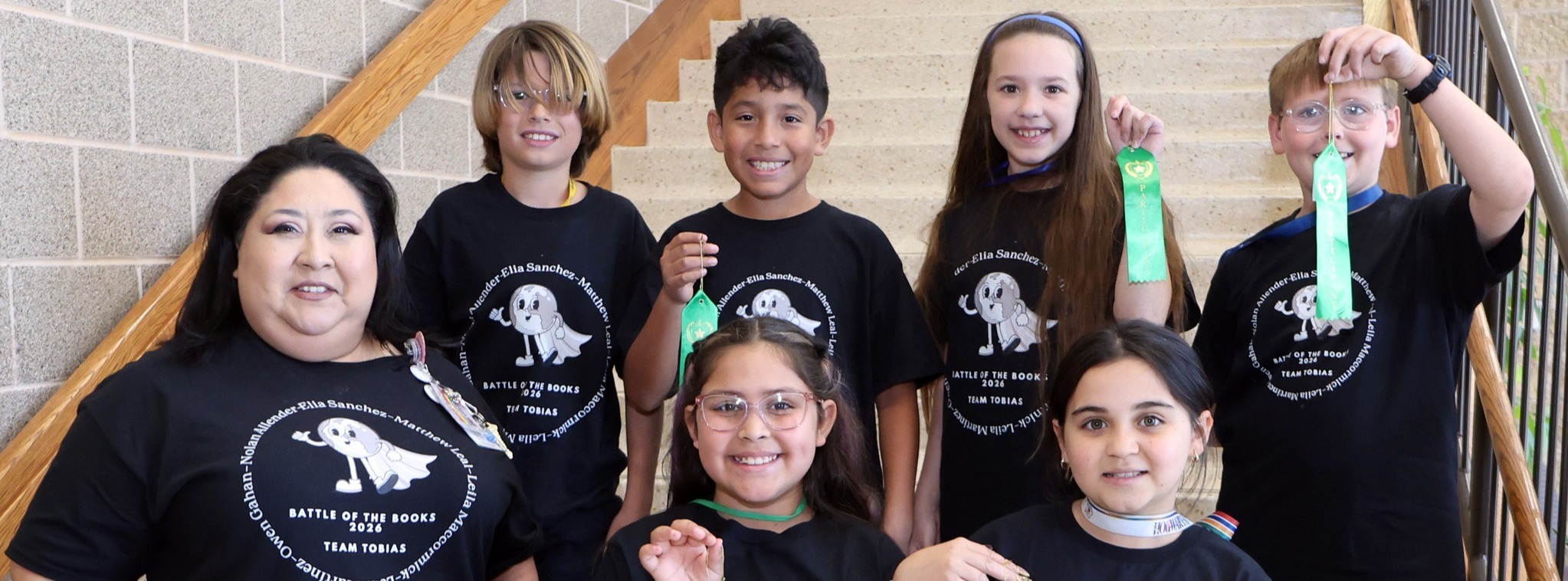 A group of six students and a teacher wearing matching shirts smiling at the camera while some students show of their green ribbon.
