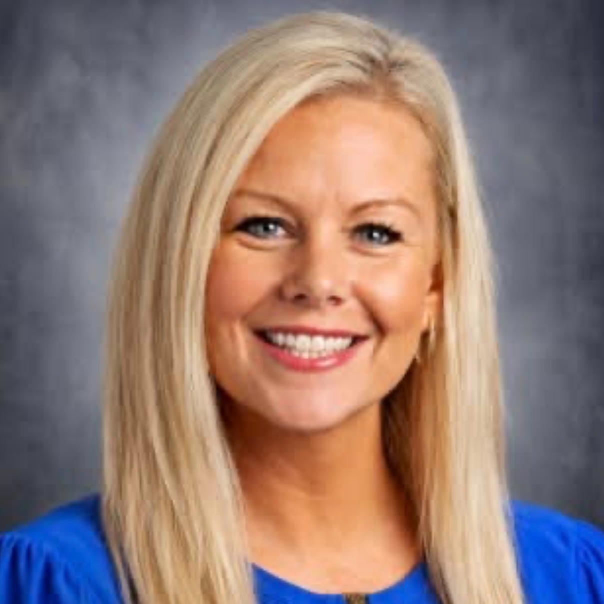 A woman with long blonde hair smiling while in front of gray professional background
