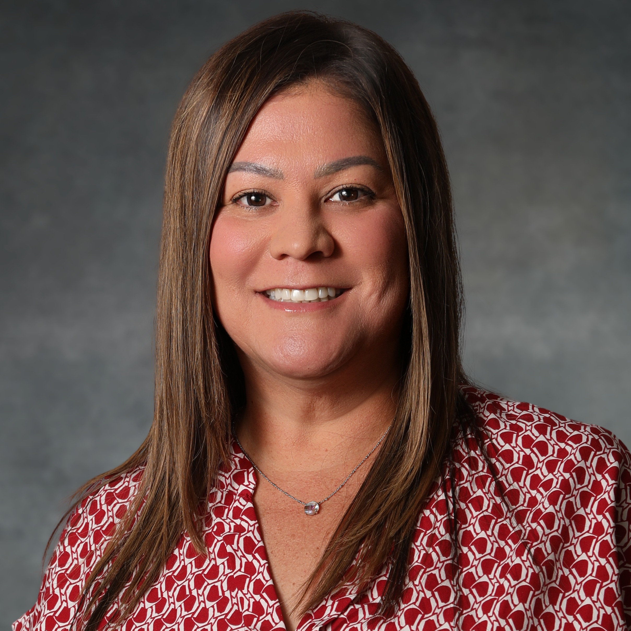 A woman with dark brown hair, wearing a red and white shirt while smiling.