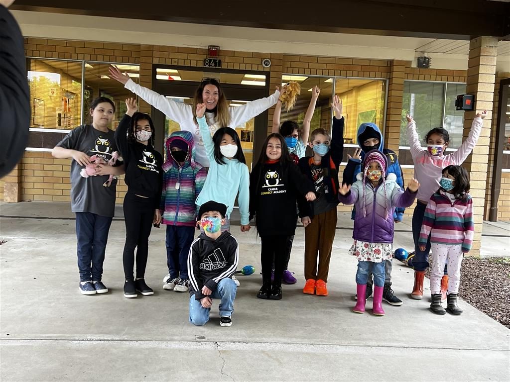 A group of children wearing face masks, posing for a photo in front of a school building.