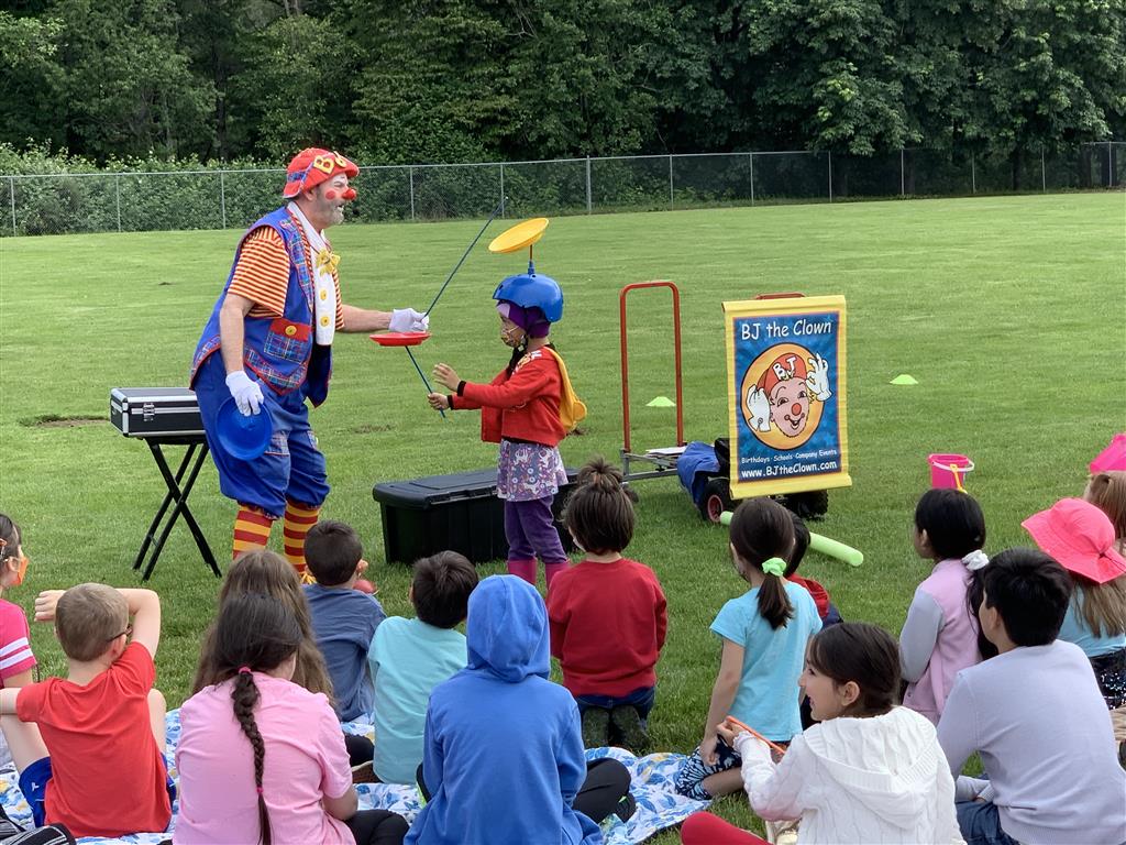 A man in a clown costume is performing for an audience of children, holding a frisbee.