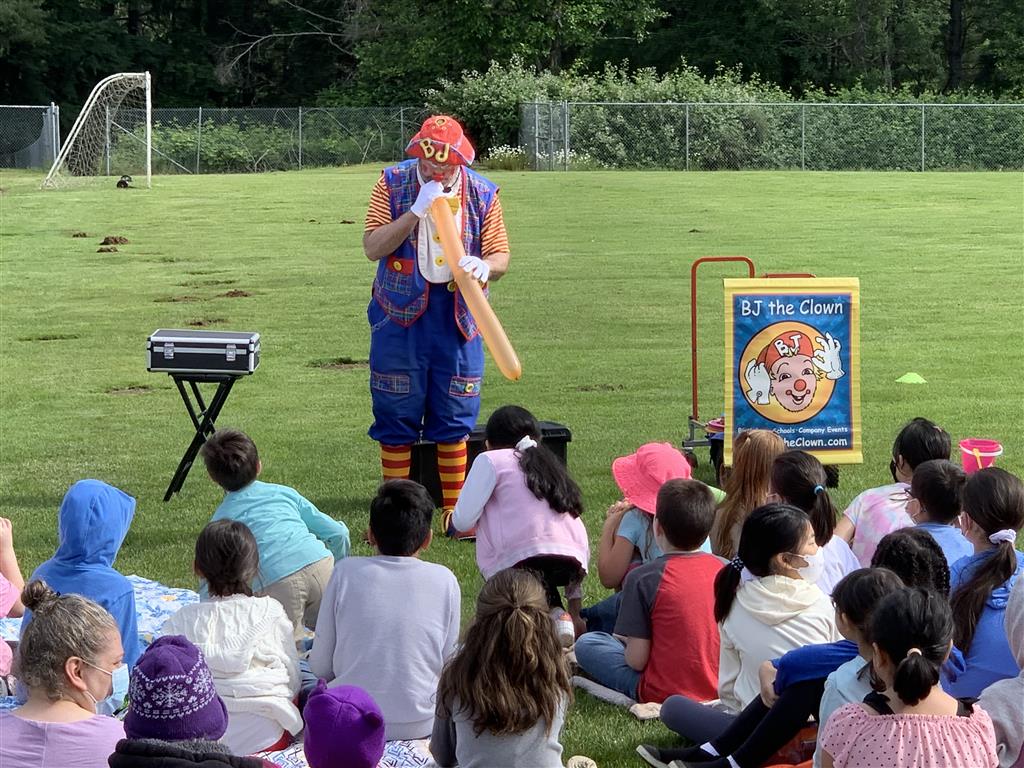 A clown in a schoolyard, performing for the children.
