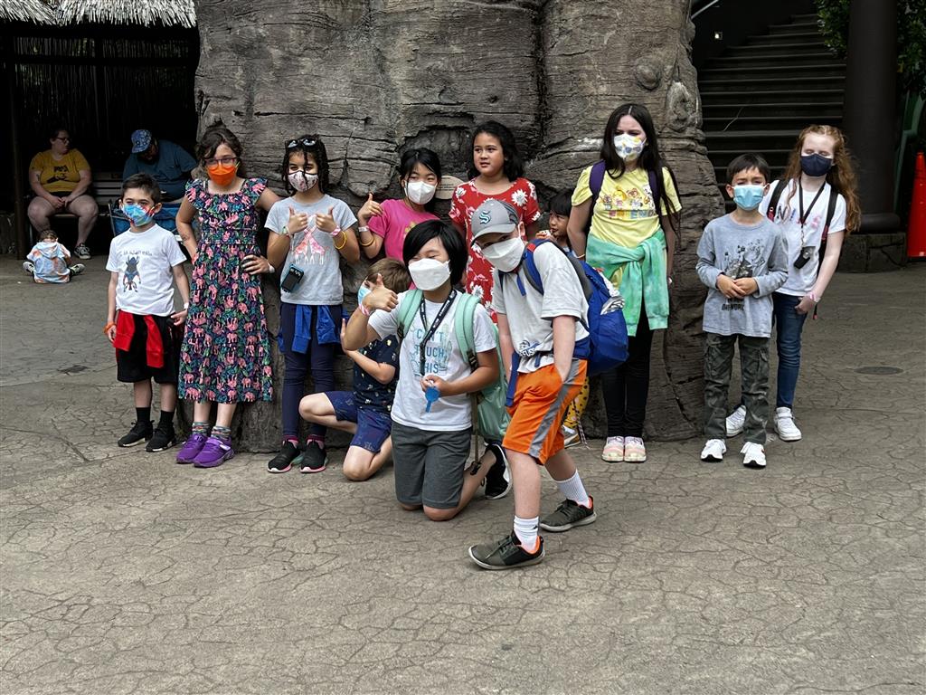 A group of children wearing masks, standing together in front of a rock wall.