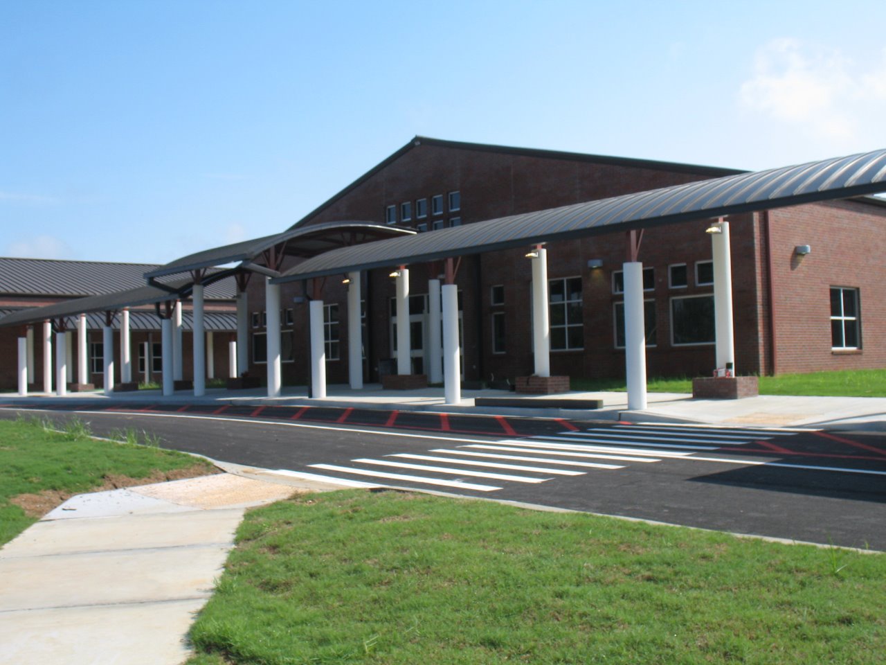A modern school building featuring a wide entrance with columns, a sloped roof, and a landscaped area in front.